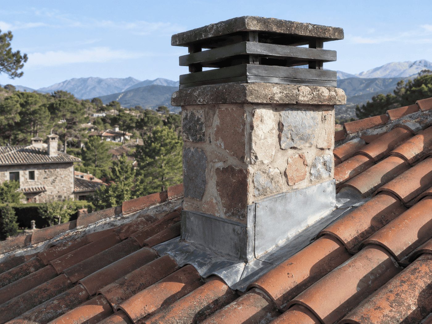 Chimenea de piedra en un tejado de la Sierra de Madrid con babero metálico de impermeabilización en su base — trabajo de reparaciondetejados.madrid.